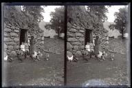 Mulher e duas meninas junto a um edifício de pedra com cobertura de colmo, em local não identificado