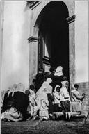 Grupo de pessoas na porta de igreja ou capela não identificada, durante a celebração da missa, na Ilha da Madeira