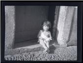 Retrato de uma bebé, sentada na soleira de uma porta, em local não identificado, na Ilha da Madeira