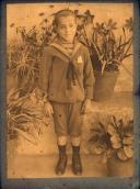 Retrato de um menino no pátio de uma casa, em local não identificado (corpo inteiro)
