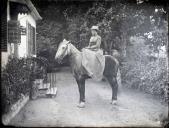 Retrato de mulher a cavalo em frente da entrada de uma casa em local não identificado