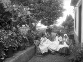 Grupo de mulheres, uma adulta e três jovens, a bordar no terreiro de um edifício, em local não identificado, na ilha da Madeira