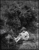 Retrato de um menino sentado junto a curso de água, em local não identificado