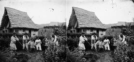 Retrato de um grupo de seis homens e uma criança no exterior de uma casa com cobertura de colmo em local não identificado, na Ilha da Madeira