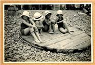 Retrato de quatro crianças, sentadas num estrado circular de madeira, no calhau da praia do Funchal, Freguesia da Sé, Concelho do Funchal]