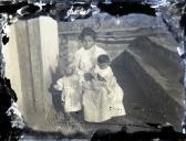 Retrato de uma mulher e duas crianças, no pátio de uma casa, em local não identificado