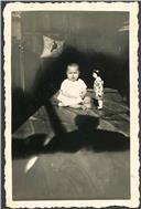 Retrato da menina Maria Vera sentada com uma boneca no interior de uma casa em local não identificado 