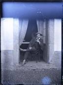 Retrato de homem sentado à porta de uma casa (corpo inteiro)