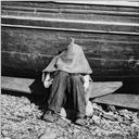 Homem sentado e encostado a um barco [na praia da cidade do Funchal]