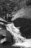Homem, com uma espingarda, junto de uma cascata na Serra da Estrela
