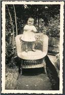 Retrato da menina Maria Vera em cima de uma cadeira de vimes no jardim de uma casa em local não identificado